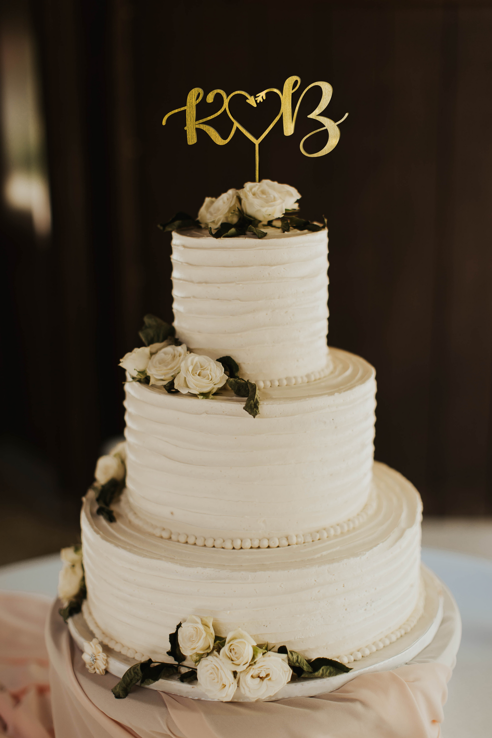 calligraphy personalized golden monogram style cake topper made of wood on top of the white simple wedding cake. 