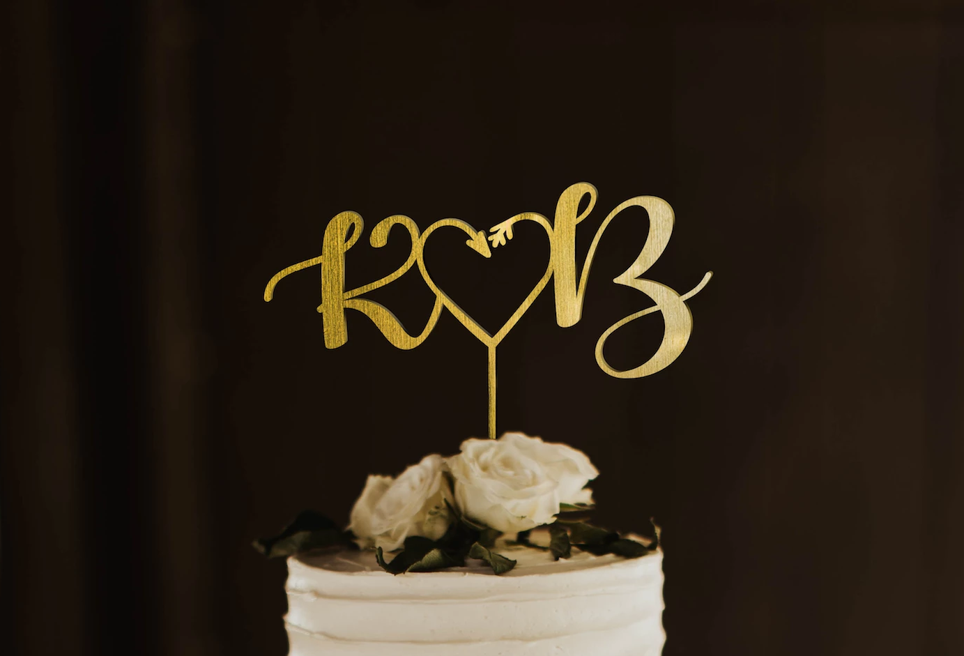 calligraphy personalized golden monogram style cake topper made of wood on top of the white simple wedding cake. 