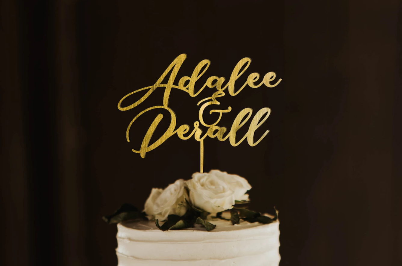 thin calligraphy personalized golden cake topper made of wood on top of the white simple wedding cake. 